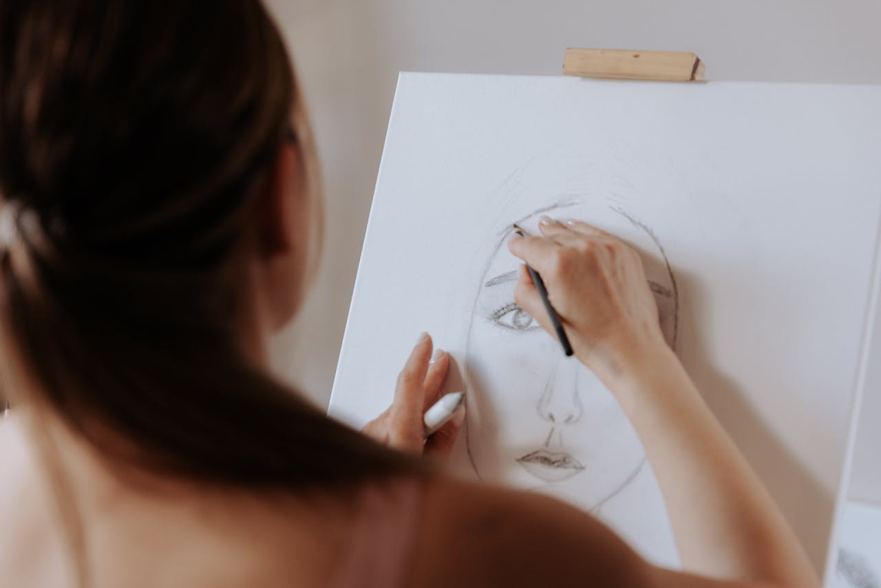 A woman focused on drawing a portrait with a pencil on a canvas, showcasing artistic concentration.