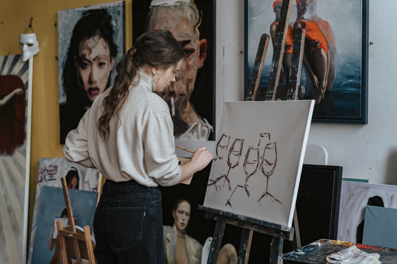 A woman artist paints wine glasses on canvas in a creative studio setting.